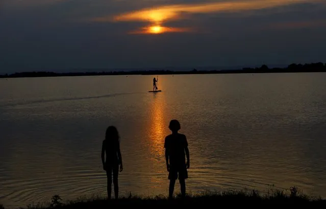 Two children are silhouetted as they observe a person on a stand up board during sunset on Lake Zicksee in St. Andrae, Austria, July 24, 2015. (Photo by Leonhard Foeger/Reuters)