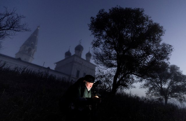 A photographer uses his mobile phone near The Church of the Kazan Icon of the Mother of God in the morning mist at dawn in the village of Osenevo, Yaroslavl region, Russia, on October 6, 2024. (Photo by Maxim Shemetov/Reuters)