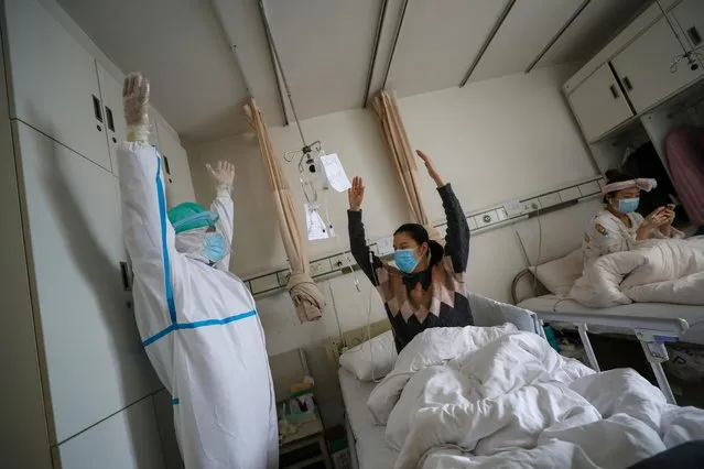 A medical worker in a protective suit shows a patient gestures of an exercise for rehabilitation at a ward of Wuhan Red Cross Hospital in Wuhan, February 24, 2020. (Photo by Reuters/China Daily)