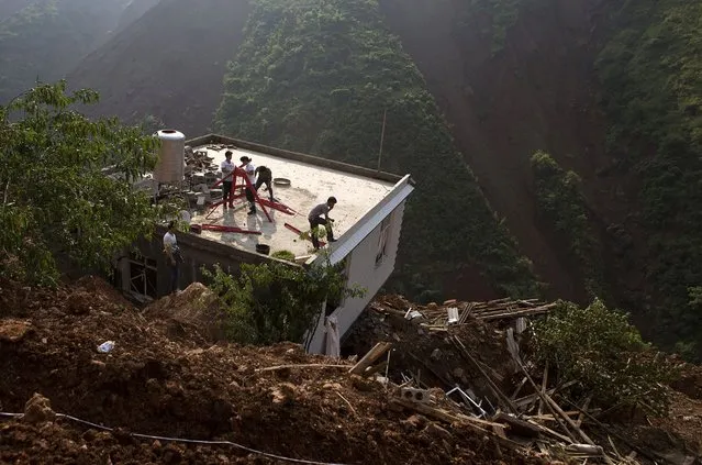People stand atop of the roof of a damaged house seen among debris after an earthquake hit Ludian county in Yunnan province August 7, 2014. The earthquake in China on the weekend triggered landslides that have blocked rivers and created rapidly growing bodies of water that could unleash more destruction on survivors of the disaster that killed 615 people, state media reported on Thursday. (Photo by Reuters/Stringer)