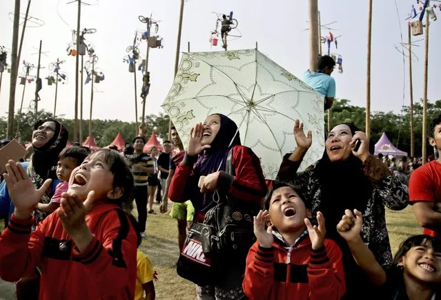 Indonesian women and children shout supports for family members who participate in a greased-pole climbing competition held as a part of the independence day celebrations in Jakarta, Indonesia, Sunday, August 17, 2014. (Photo by Dita Alangkara/AP Photo)