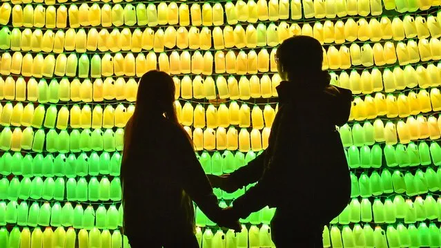 People hold hands in front of an art installation title MilkBottle Screen, which is made of 600 one pint milk bottles on display in Castle Park, Bristol on February 28, 2020, as part of the first ever Bristol Light Festival. (Photo by Ben Birchall/PA Images via Getty Images)