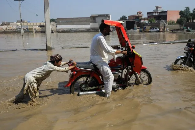 A boy pushes a motorbike after it stopped amid flood water, following rains and floods during the monsoon season in Nowshera, Pakistan on August 30, 2022. (Photo by Fayaz Aziz/Reuters)