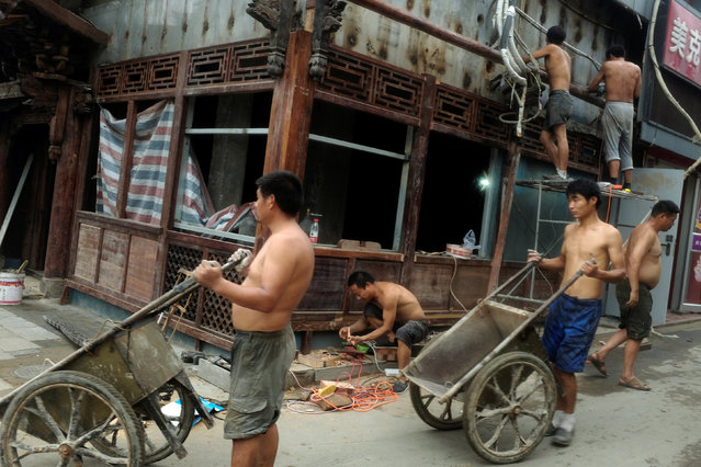 Men push wheel barrows as others repair a shop front in a hutong, or alley, in Beijing, China, July 30, 2016. (Photo by Thomas Peter/Reuters)