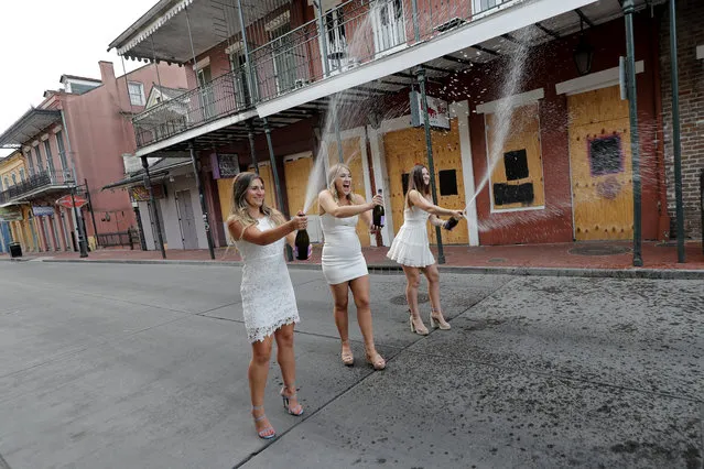 Tulane University graduates pop prosecco as they pose for graduation photos on a largely empty Bourbon Street, due to the coronavirus pandemic, in the French Quarter of New Orleans, Tuesday, May 12, 2020. (Photo by Gerald Herbert/AP Photo)