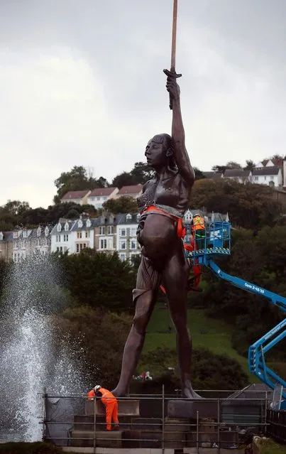 Contractors move Damien Hirst's bronze sculpture of a pregnant woman into position on the harbour wall on October 16, 2012 in Ilfracombe, England. The bronze-clad, sword-wielding 65ft (20m) statue, named Verity, has been controversially given to the seaside town by the artist, on a 20-year loan and was erected by crane on the pier.  (Photo by Matt Cardy)