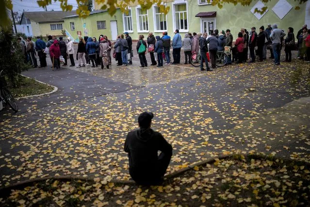 A man sits as people queue to receive a daily ration of bread in a school in Mykolaiv, Tuesday, October 25, 2022. Mykolaiv residents pick up bread from the only food distribution point in Varvarivka, a Mykolaiv district where thousands of people live. One person is allowed to receive free bread just once in three days. (Photo by Emilio Morenatti/AP Photo)