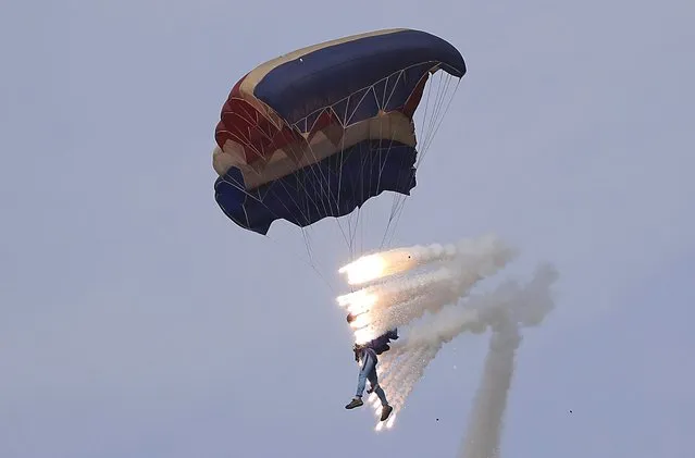 Pyrotechnics explode as a military parachutist descends upon Kalma Airport on Sunday, September 25, 2016, in Wonsan, North Korea. Thousands of Koreans and hundreds of foreign tourists and journalists invited to Wonsan, a port city, for the Wonsan International Friendship Air Festival, were given a glimpse of North Korea's own Air Force fighters, remote-controlled scale mock-up planes including an F-16 fighter jet, and demonstrations of military parachuting, with the first two skydivers descending with huge North Korean and ruling party flags. (Photo by Wong Maye-E/AP Photo)