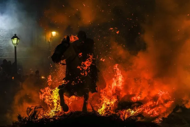A man rides a horse through a bonfire as part of a ritual in honor of Saint Anthony the Abbot, the patron saint of domestic animals, in San Bartolome de Pinares, Spain, Monday, January 16, 2023. On the eve of Saint Anthony's Day, dozens ride their horses through the narrow cobblestone streets of the small village of San Bartolome during the “Luminarias”, a tradition that dates back 500 years and is meant to purify the animals with the smoke of the bonfires and protect them for the year to come. (Photo by Manu Fernandez/AP Photo)