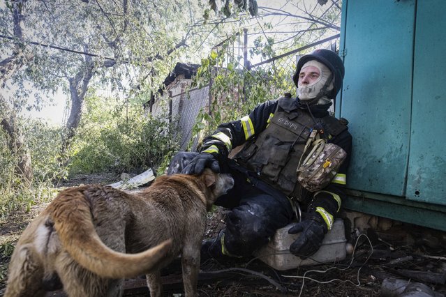 A firefighter pets a dog as he rests after putting out a fire in a private house hit by Russian shelling in Kharkiv, Ukraine, Friday, May 3, 2024. (Photo by Yevhen Titov/AP Photo)