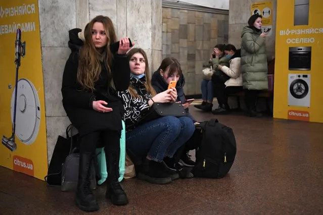 Girls hold their mobile phone as they take refuge in a metro station in Kyiv in the morning of February 24, 2022. Air raid sirens rang out in downtown Kyiv today as cities across Ukraine were hit with what Ukrainian officials said were Russian missile strikes and artillery. (Photo by Daniel Leal/AFP Photo)