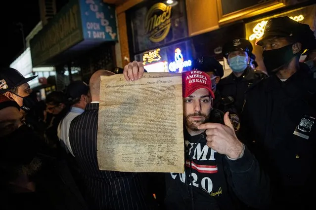 A man holds a copy of the Declaration of Independence while people protest outside of the Mac's Public House after it closed down amid the coronavirus disease (COVID-19) pandemic in the Staten Island borough of New York City, U.S., December 2, 2020. (Photo by Jeenah Moon/Reuters)