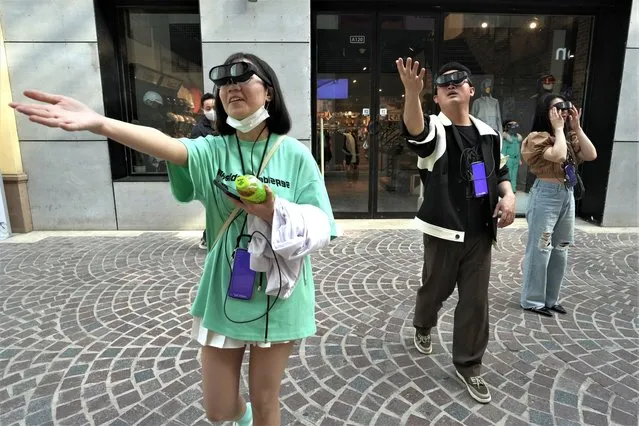 Visitors to a mall grasp at air as they try out an augmented reality experience of a digital art gala in Beijing, Tuesday, May 2, 2023. (Photo by Ng Han Guan/AP Photo)