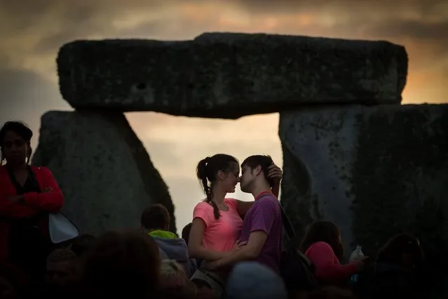 A young couple kiss at Stonehenge during a sunset ceremony as thousands of people flock to the prehistoric monument to celebrate summer solstice, on June 21, 2013. Salisbury Plain, Wiltshire. (Photo by SWNS)