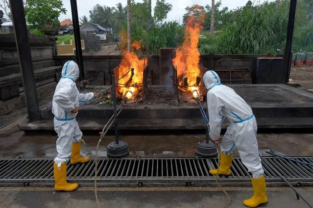 Officials wearing personal protective equipment (PPE) set fires to bodies of people who died due to the coronavirus at a crematorium in Bangli, Bali, Indonesia October 10, 2020. (Photo by Nyoman Hendra Wibowo/Antara Foto via Reuters)