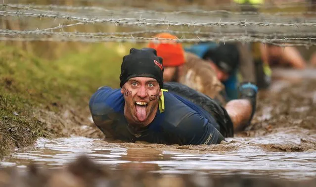 A competitor gestures as he crawls beneath barbed wire during the Tough Guy event in Perton, central England February 1, 2015. The annual event to raise cash for charity challenges thousands of international competitors in a cross country run followed by an assault course consisting of obstacles including water, fire and tunnels. (Photo by Phil Noble/Reuters)