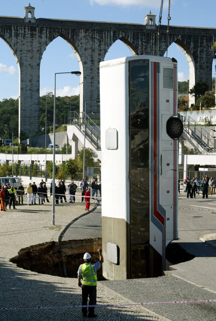Rescue workers remove a bus with a crane from a Lisbon street hole November 25, 2003. The bus was parked on a Lisbon street when the ground began to open up and gobble it. No casualties were registed. (Photo by Jose Manuel/Reuters)