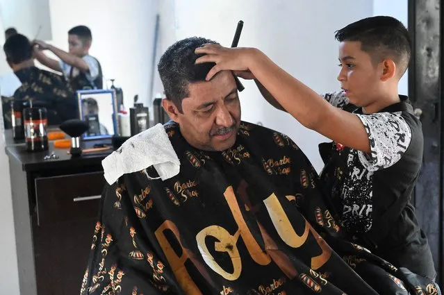 Eduardo Espinal, a 12-year-old child, cuts the hair of a client at his barbershop in Comayagua, Honduras, on August 9, 2022. With scissors and a desire to excel, 12-year-old Eduardo Espinal makes his way with his barbershop in Honduras, one of the oldest trades in the world, to escape economic difficulties and the “American dream”. (Photo by Orlando Sierra/AFP Photo)
