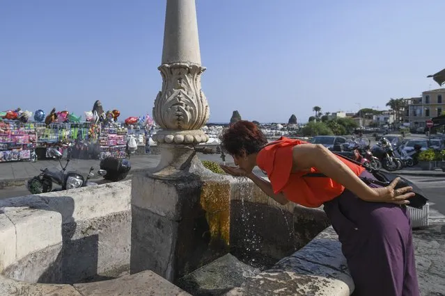 A woman refreshes herself at a fountain in Aci Trezza, near Catania, Sicily, Italy, Friday, August 13, 2021. Stifling heat is gripping much of Italy and Southern Europe, with peak temperatures reaching over 40 degrees Celsius (104 degrees Fahrenheit) and forecasters sayin worse is expected to come. (Photo by Salvatore Cavalli/AP Photo)