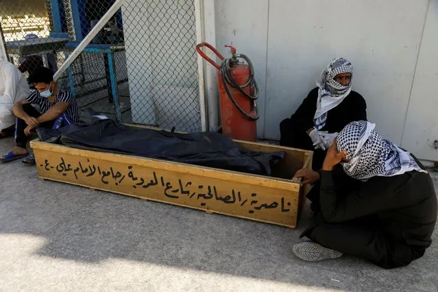 People sit near a coffin with a body bag containing the remains of a victim after a fire broke out at al-Hussain coronavirus hospital in Nassiriya, Iraq, July 13, 2021. The death toll from a fire that tore through a coronavirus hospital in southern Iraq rose to 66, health officials said on Tuesday, as authorities faced accusations of negligence from grieving relatives and a doctor who works there. (Photo by Khalid al-Mousily/Reuters)