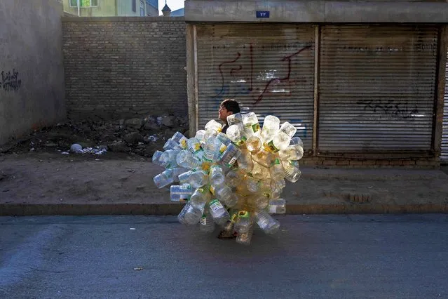An Afghan boy carrying empty plastic cans, walks along a street in Kabul on December 21, 2023. (Photo by Wakil Kohsar/AFP Photo)