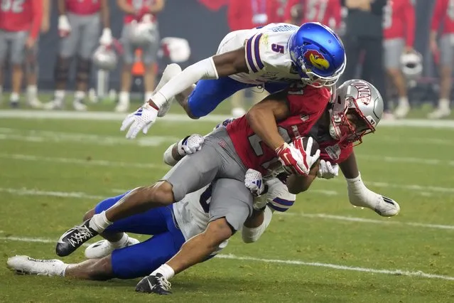 UNLV wide receiver Jacob De Jesus is tackled by Kansas safety O.J. Burroughs (5) and linebacker Taiwan Berryhill Jr. during the first half of the Guaranteed Rate Bowl NCAA college football game Tuesday, December 26, 2023, in Phoenix. (Photo by Rick Scuteri/AP Photo)