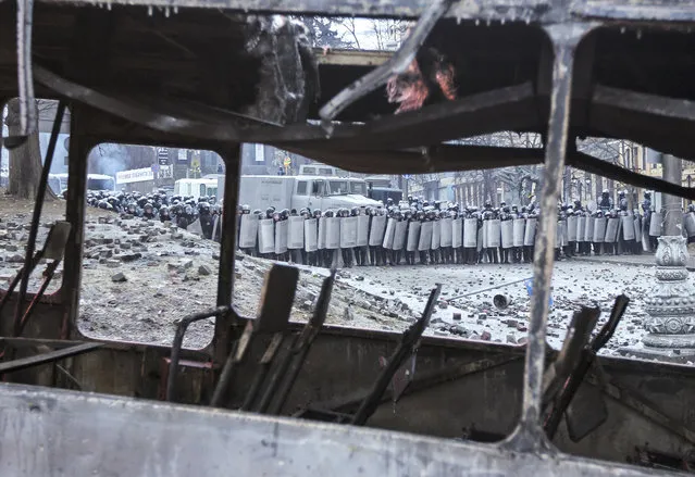 Ukrainian riot police take cover behind their shields in front of a burned bus during a continued protest near government administration buildings in Kiev, on January 20, 2014. (Photo by Valentyn Ogirenko/Reuters)