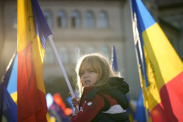 A little girl waves a flag during an anti-government and anti-restrictions protest organised by the far-right Alliance for the Unity of Romanians or AUR, in Bucharest, Romania, Saturday, October 2, 2021. Thousands took to the streets calling for the government's resignation, as Romania reported 12.590 new COVID-19 infections in the past 24 hour interval, the highest ever daily number since the start of the pandemic. (Photo by Vadim Ghirda/AP Photo)