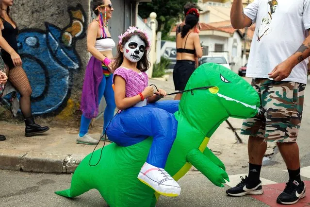 A participant rides on an inflatable dinosaur during a street parade called “Cumbia Calavera”, made up of immigrants and non-immigrants who venerate the life and also the death of their loved ones in Sao Paulo, Brazil, 18 February 2024. (Photo by Isaac Fontana/EPA)