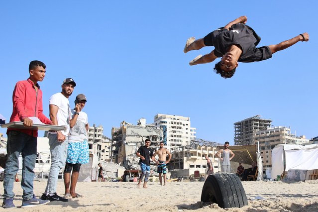 People watch as a young Palestinian performs an acrobatic jump on the beach, during soaring summer temperatures in Gaza City on June 14, 2024, amid the ongoing conflict between Israel and the Palestinian Hamas militant group. (Photo by Omar Al-Qattaa/AFP Photo)