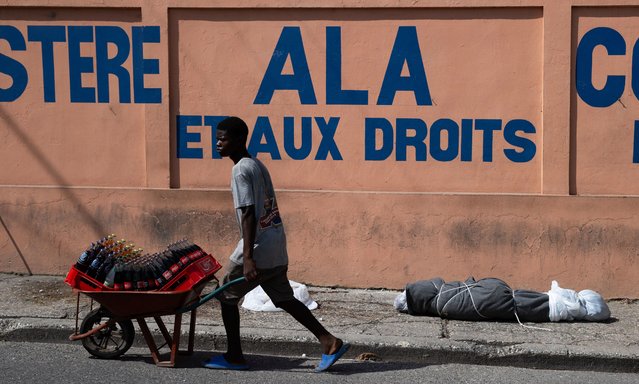 People walk in front of a body which was left wrapped in plastic and tied, on a street near the National Palace in Port-au-Prince, Haiti, 27 May 2024. According to the United Nations Integrated Office in Haiti, last year alone, violence caused at least 8,000 victims in Haiti, where gangs control much of Port-au-Prince and other areas of the country. (Photo by Orlando Barría/EPA/EFE)