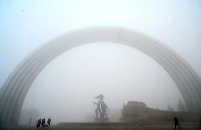 People walk next to a Soviet Era monument during heavy fog in the center of Ukrainian capital of Kiev on October 24, 2019. (Photo by Sergei Supinsky/AFP Photo)