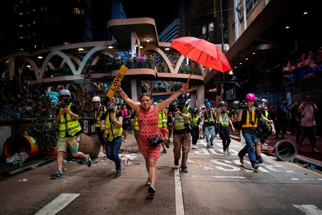 A woman holds up an umbrella and license plates, one that reads “love”, during violent protests between riot police and demonstrators in the Causeway Bay district of Hong Kong on October 1, 2019. The city observes the National Day holiday to mark the 70th anniversary of communist China's founding Strife-torn Hong Kong on October 1 marked the 70th anniversary of communist China's founding with defiant “Day of Grief” protests and fresh clashes with police as pro-democracy activists ignored a ban and took to the streets across the city. (Photo by Nicolas Asfouri/AFP Photo)