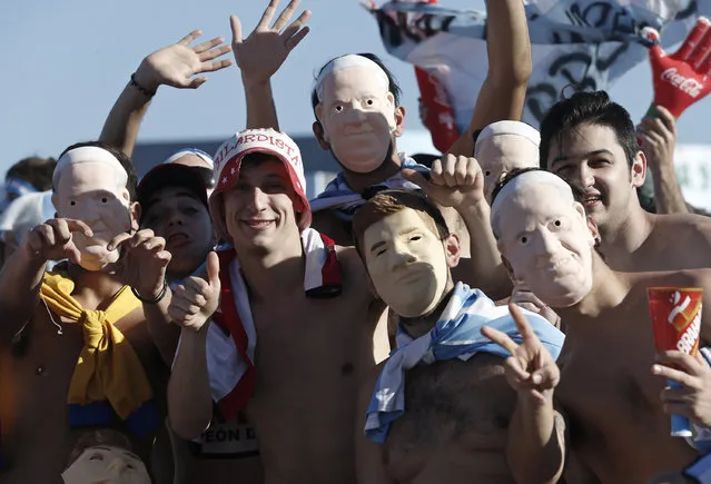 Argentina soccer fans wearing masks of player Lionel Messi and Pope Francis pose for photos before watching the World Cup final match between Argentina and Germany, via live telecast on Copacabana beach in Rio de Janeiro, Brazil, Sunday, July 13, 2014. (Photo by Silvia Izquierdo/AP Photo)