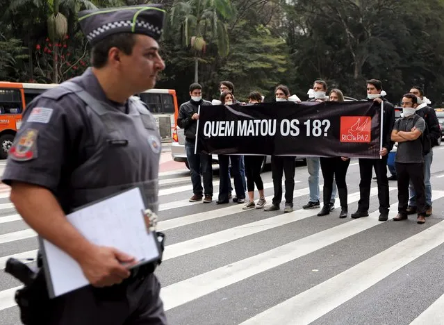 A police officer walks past activists of NGO “Rio da Paz” who are attending a demonstration in solidarity with relatives of victims of the 18 people killed last week at Paulista Avenue in Sao Paulo's financial centre, Brazil, August 20, 2015. Brazilian police are investigating whether a string of 18 murders in metropolitan Sao Paulo on August 13 night were a coordinated act of revenge by off-duty officers following the nearby deaths of two colleagues in the previous week. (Photo by Paulo Whitaker/Reuters)