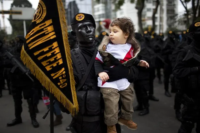 Intor Montoro Carba, 20, a military special forces officer, holds Jeremy Bock, at the request of Jeremy's parents who wanted to make a photo of their son with the striking soldier, before the start of a military parade marking the country's Independence Day in Lima, Peru, Friday, July 29, 2016. Peru declared it's independence from Spain in 1821. (Photo by Rodrigo Abd/AP Photo)