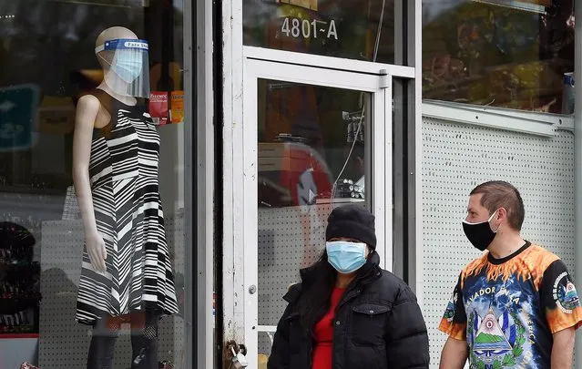 People with face masks to protect themselves from the coronavirus walk past a shop window displaying a manequin wearing a mask and face shield on April 18, 2020, in Arlington, Virginia. (Photo by Olivier Douliery/AFP Photo)