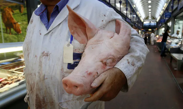 In this photo taken on Monday, July 18, 2016, a butcher carries a pigs head at Smithfield Market in London. Welsh farmers like Rees Roberts, who have 1,000 acres with sheep, cattle and crops, can expect to earn a premium on their meats thanks to a certificate of regional authenticity. But that marker of distinction – the same kind that ensures Champagne can only come from the French region of the same name – is granted by the European Union and is now at risk after Britain voted to leave the 28-country bloc. (Photo by Kirsty Wigglesworth/AP Photo)