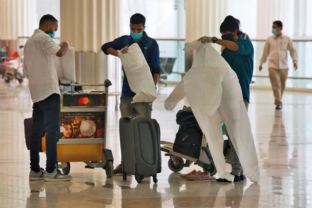 Passengers wearing masks due to the coronavirus pandemic put on throwaway coveralls before their flight at Dubai International Airport's Terminal 3 in Dubai, United Arab Emirates, Wednesday, June 10, 2020. The coronavirus pandemic has hit global aviation hard, particularly at Dubai International Airport, the world's busiest for international travel, due to restrictions on global movement over the virus. (Photo by Jon Gambrell/AP Photo)