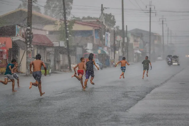 Boys run along a road during a downpour amid the coronavirus pandemic in Santo Tomas, Pampanga province, Philippines, 24 May 202​0. (Photo by Mark R. Cristino/EPA/EFE)