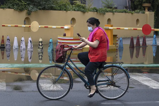 A woman wearing a mask to curb the spread of the coronavirus cycle along a street after a downpour in Beijing on Thursday, June 25, 2020. In China, where the virus first appeared late last year, an outbreak in Beijing appeared to have been brought under control. China reporting more than a dozen of newly confirmed cases nationwide amid mass testing in the capital. (Photo by Ng Han Guan/AP Photo)