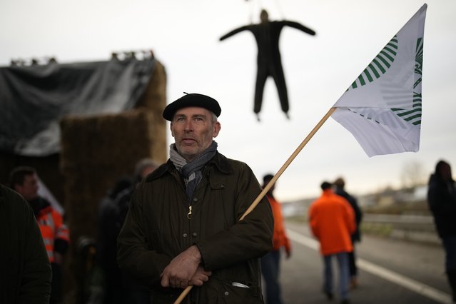 A farmer stands at a barricade as farmers block a highway Tuesday, January 30, 2024 in Jossigny, east of Paris. With protesting farmers camped out at barricades around Paris, France's government hoped to calm their anger with more concessions Tuesday to their complaints that growing and rearing food has become too difficult and not sufficiently lucrative. (Photo by Christophe Ena/AP Photo)