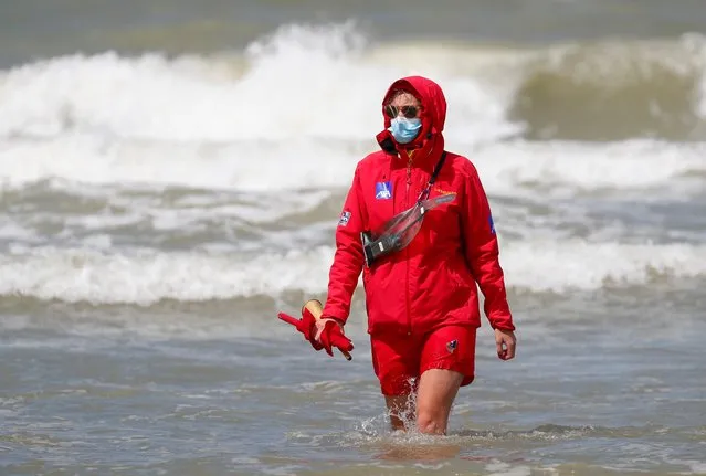 A lifeguard wearing a protective face mask walks through North Sea waters as Belgian coastal towns impose masks on dykes amid the coronavirus disease (COVID-19) outbreak in Ostend, Belgium on July 28, 2020. (Photo by Francois Lenoir/Reuters)