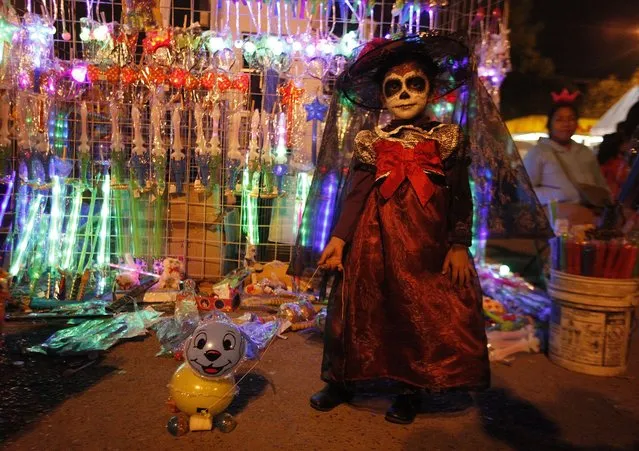 Kimberli, 4, dressed up with her face painted as the popular Mexican figure “Catrina”, poses for a photograph with her plastic dog in front of a street vendor's stall in Ciudad Juarez late November 2, 2014. The character “Catrina”, also known as the “The Elegant Death”, was created by Guadalupe Posada in the early 1900s and has become an important part of Mexico's celebrations of the Day of the Dead on November 1 and 2. (Photo by Jose Luis Gonzalez/Reuters)