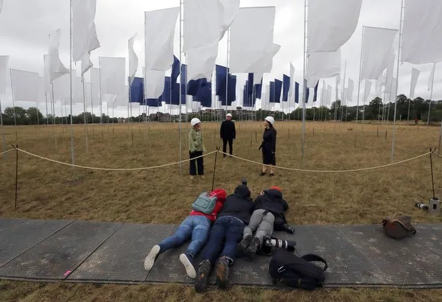 Photographers lie on the ground to take the best picture as Nurse Angela Helleur, right, is guided through Luke Jerram's In Memoriam art installation that was erected outside the Queen Elizabeth Hospital on Woolwich Common in London, Saturday, August 29, 2020. It has been created as a memorial to those lost in the Covid-19 pandemic as well a tribute to the NHS and care-workers. Created from bed sheets, In Memoriam is intended to be an evocative symbol of local, national and international solidarity, presented as a space for reflection, remembrance, and recognition. (Photo by Frank Augstein/AP Photo)