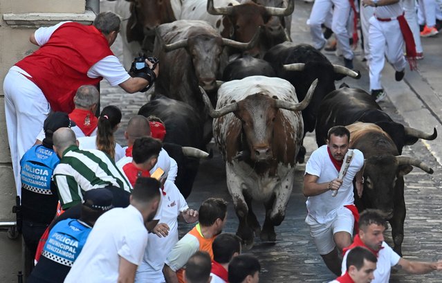 Participants run ahead of La Palmosilla breed bulls during the seventh running of the bulls of the San Fermin festival in Pamplona, northern Spain, on July 13, 2025. Thousands of people every year attend the week-long festival and its famous “encierros” or bull runs, every day at 8:00 a.m. through the narrow streets of the old town over an 850 meters (yard) course while runners ahead of them try to stay close to the bulls without falling over or being gored. (Photo by Miguel Riopa/AFP Photo)