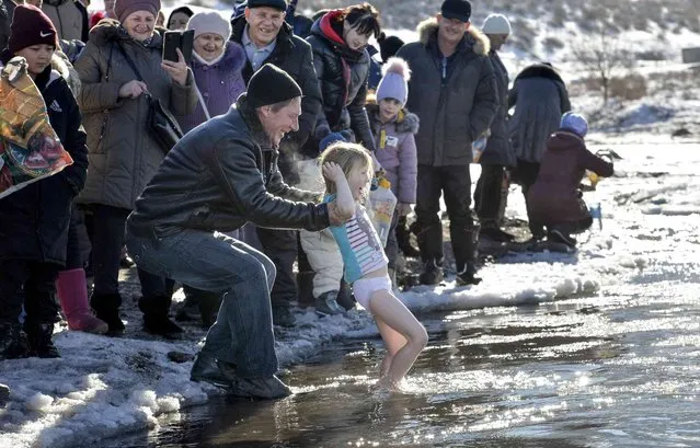 A man bathes his daughter in water during a traditional Epiphany celebration in the mountain river Kara-Balta, during celebration a traditional Epiphany near Sosnovka village, 90 km (56 miles), southwest of Bishkek, Kyrgyzstan, Thursday, January 19, 2023. (Photo by Vladimir Voronin/AP Photo)