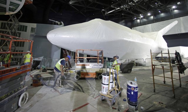 Workers vacuum up debris and move construction materials in an area inside a building where space shuttle Atlantis, wrapped in protective plasitc, will go on exhibit at the Kennedy Space Center Visitor Complex, Thursday, April 11, 2013, in Cape Canaveral, Fla. The plastic wrap is scheduled to be removed in several weeks and the exhibit will be open to the public on June 29. (Photo by John Raoux/AP Photo)