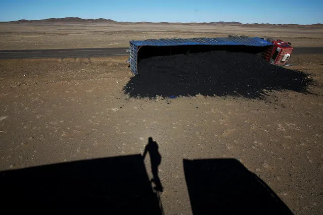 A photographer casts his shadow near a coal truck which flipped over at Khanbogd Soum, near the border with China in the Gobi desert, Mongolia, October 29, 2017. Getting to the border can be a harrowing ordeal, as vehicles speed towards China and back down the one-lane road. With no street lamps to guide the way and drink-driving a constant problem, danger levels increase at night, drivers say. (Photo by Bazarsukh Rentsendorj/Reuters)