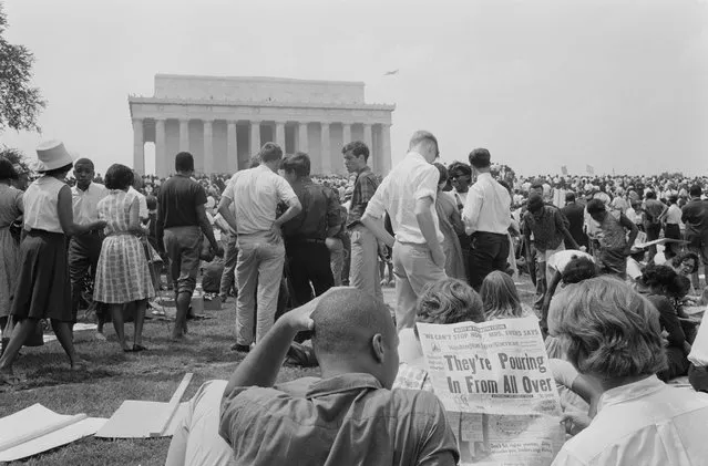 A crowd of on the grounds of the Lincoln Memorial with two men in the foreground reading a newspaper with the headline "They're Pouring In From All Over" during the civil rights march on Washington D.C., August 28, 1963. (Photo by Reuters/Library of Congress)